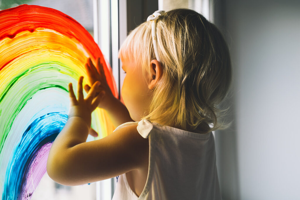 Curious child exploring colourful rainbow painting on window at Tribe Early Learning Centre